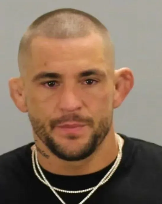Retrato tipo ficha policial de un hombre con la cabeza rapada, barba recortada y camiseta negra.