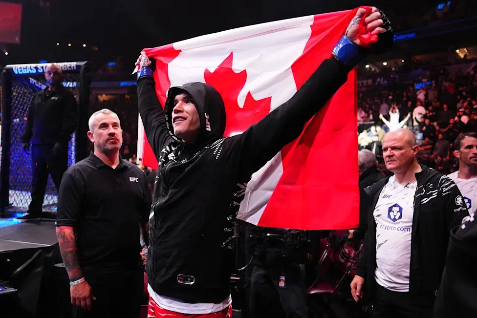 Un peleador de la UFC levanta la bandera de Canadá dentro del octágono, rodeado por su equipo.