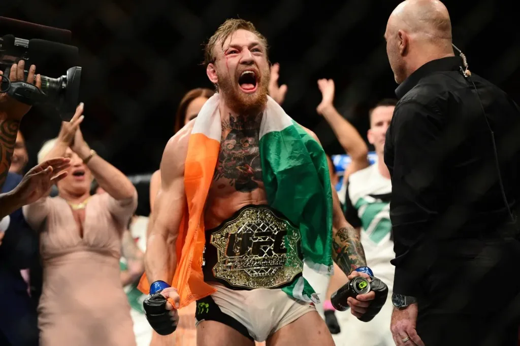 Conor McGregor celebra con la bandera de Irlanda y el cinturón de campeón de UFC tras su victoria.