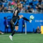 Un futbolista de negro controla el balón en pleno partido frente a la portería.
