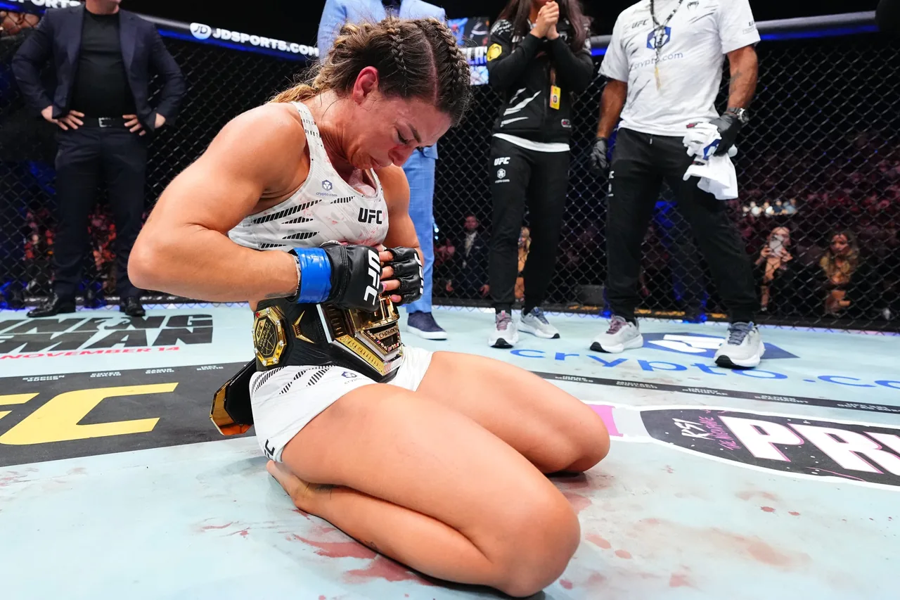 Una luchadora de UFC, arrodillada en la jaula, se quita o ajusta el cinturón de campeona tras el combate.
