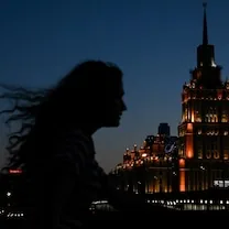Silueta de una persona con el cabello al viento frente a un edificio iluminado de noche.