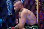 Un luchador profesional sentado en el ring, con el torso desnudo y gesto de cansancio tras el combate.